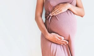Pregnant woman holds belly with both hands in pink dress