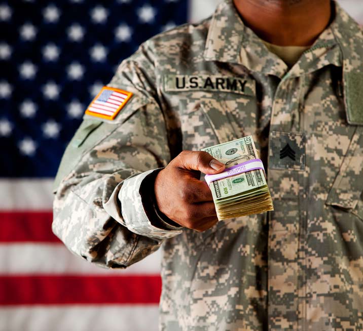 Military man holding out money in front of flag
