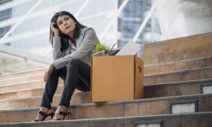 Businesswoman sitting on stairs with box of belongings after being laid off