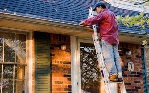 Homeowner cleaning his homes gutters on ladder