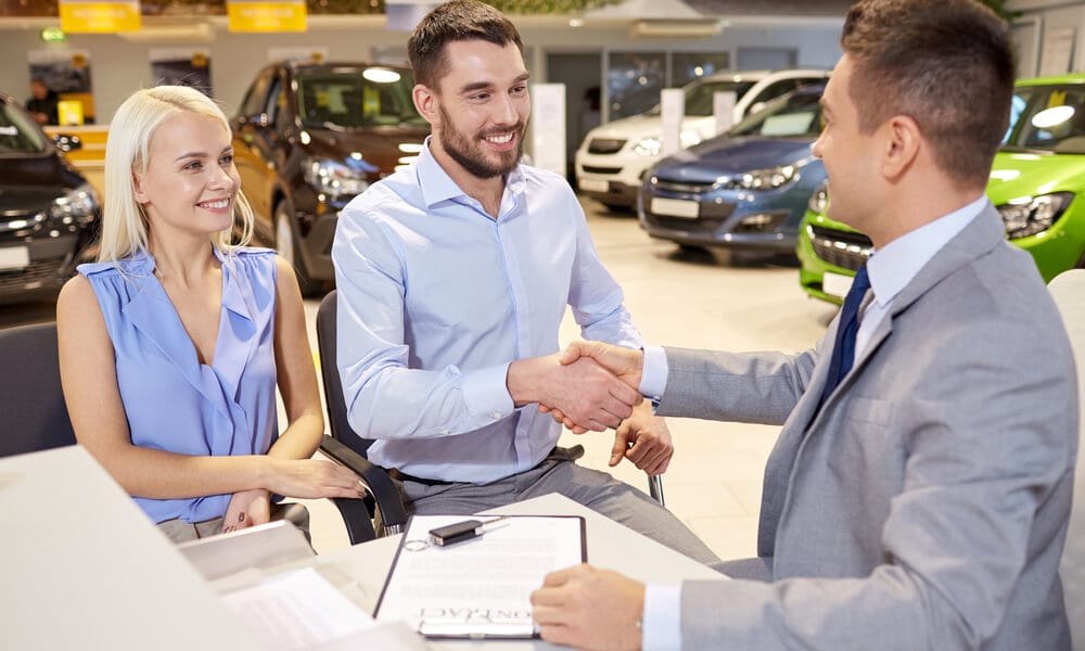Couple shaking hands with dealer in car dealership