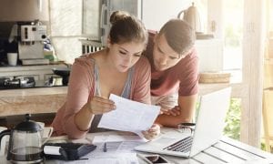 Young couple managing finances, reviewing their bank accounts using laptop computer and calculator at modern kitchen