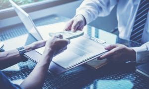 Photo of man swapping loan agreement with wad of cash from lender