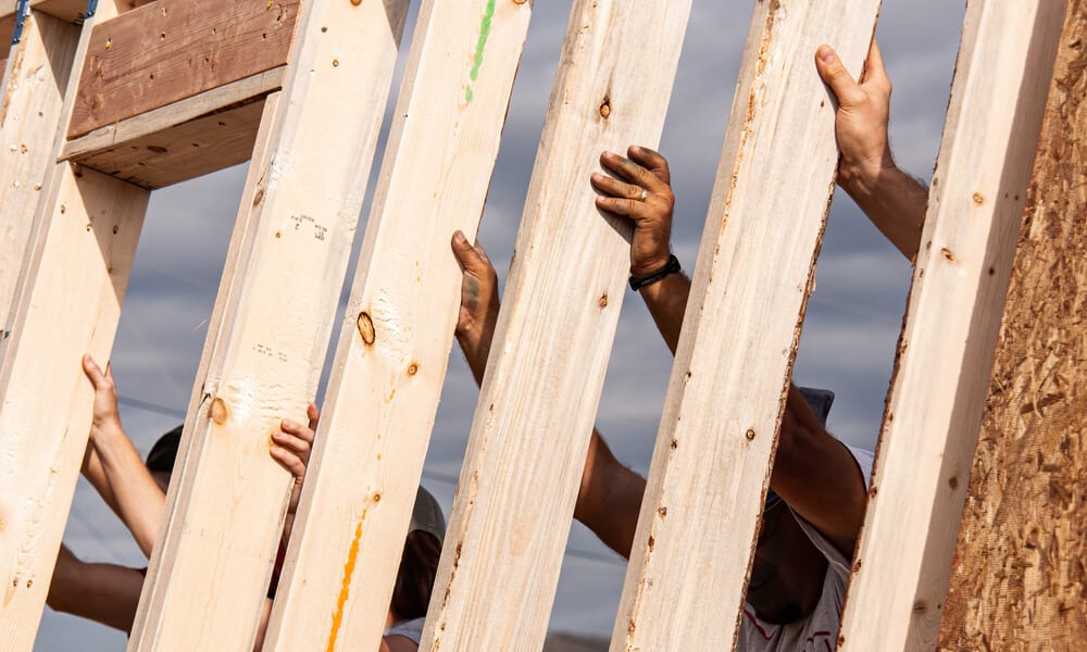 Hands of volunteers raising a wall for a Habitat for Humanity home