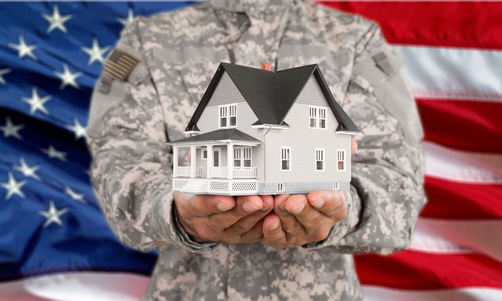 Military man holding model home in front of American flag