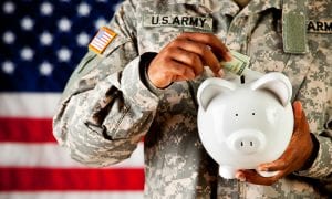 U.S Soldier putting money into white ceramic piggy bank in front of U.S flag