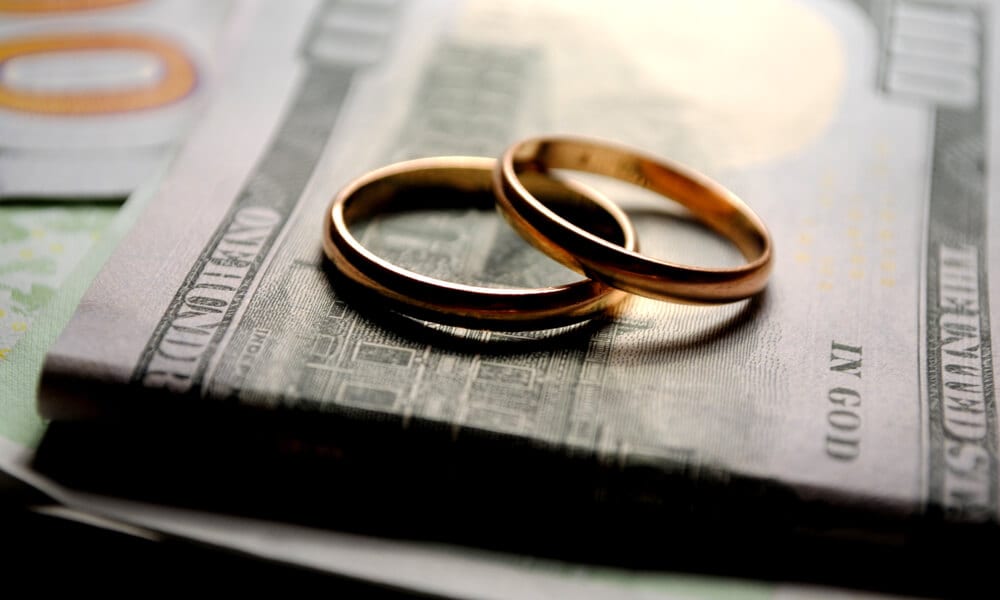 Photo of wedding rings on top of small stack of 100 dollar bills