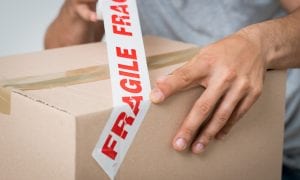 Man packing box and putting tape labeled fragile over the box