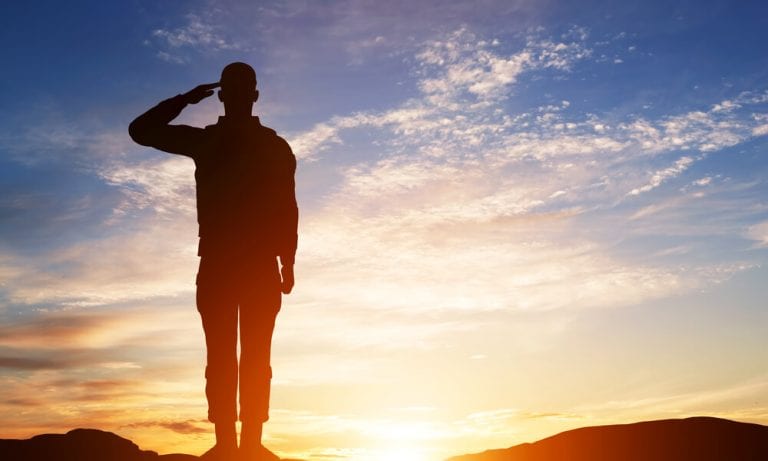 Soldier silhouette saluting on sunset background
