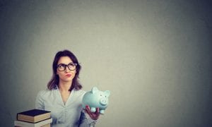 Student holding stack of books in one hand and piggy-bank in other