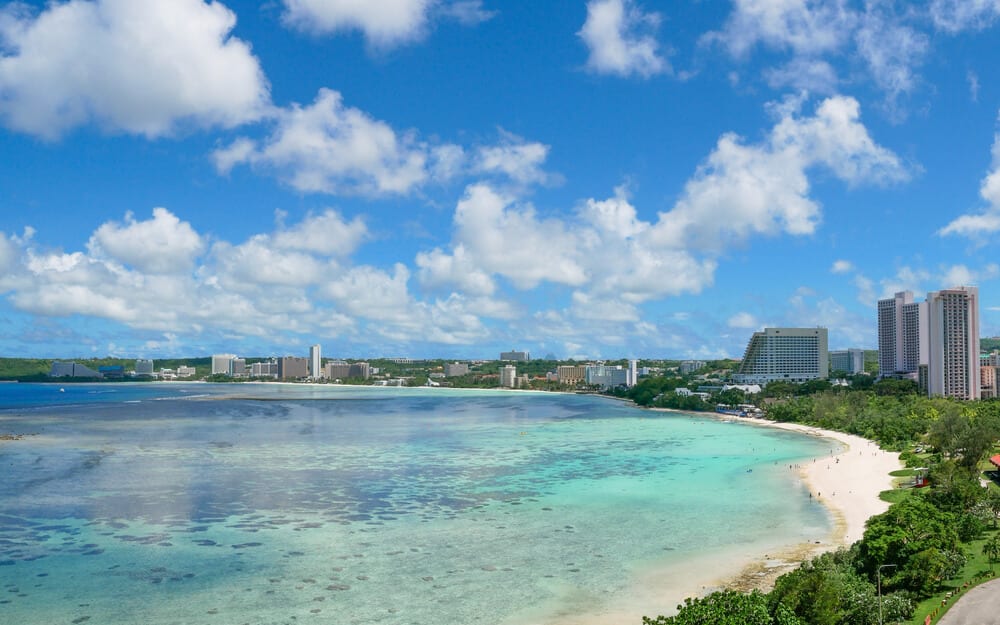 Overlook view of Tumon bay beach in Guam visible clear waters and tall buildings with lush greenery in background