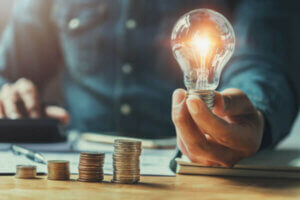 Man holding a light bulb with his savings stacked on a desk