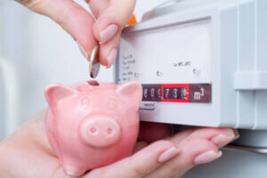 Holding a piggy bank next to the apartment's thermostat