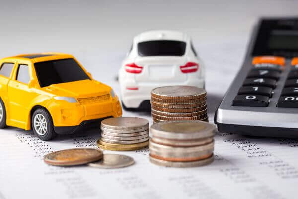 Una calculadora, monedas y carritos de juguete sobre una mesa, simbolizando pagos del carro.