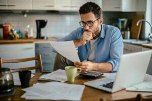Worried young man reviewing bills at his kitchen table, representing the concept of Charge-Off versus Cancellation of Debt.