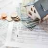 Model house on tax forms and cash, representing the process of buying a home while owing taxes.
